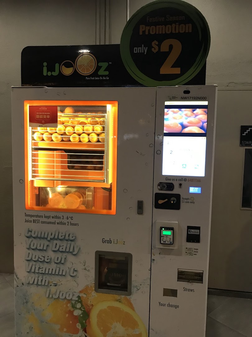 An iJooz vending machine showcasing fresh oranges and a $2 festive promotion for pure juice.