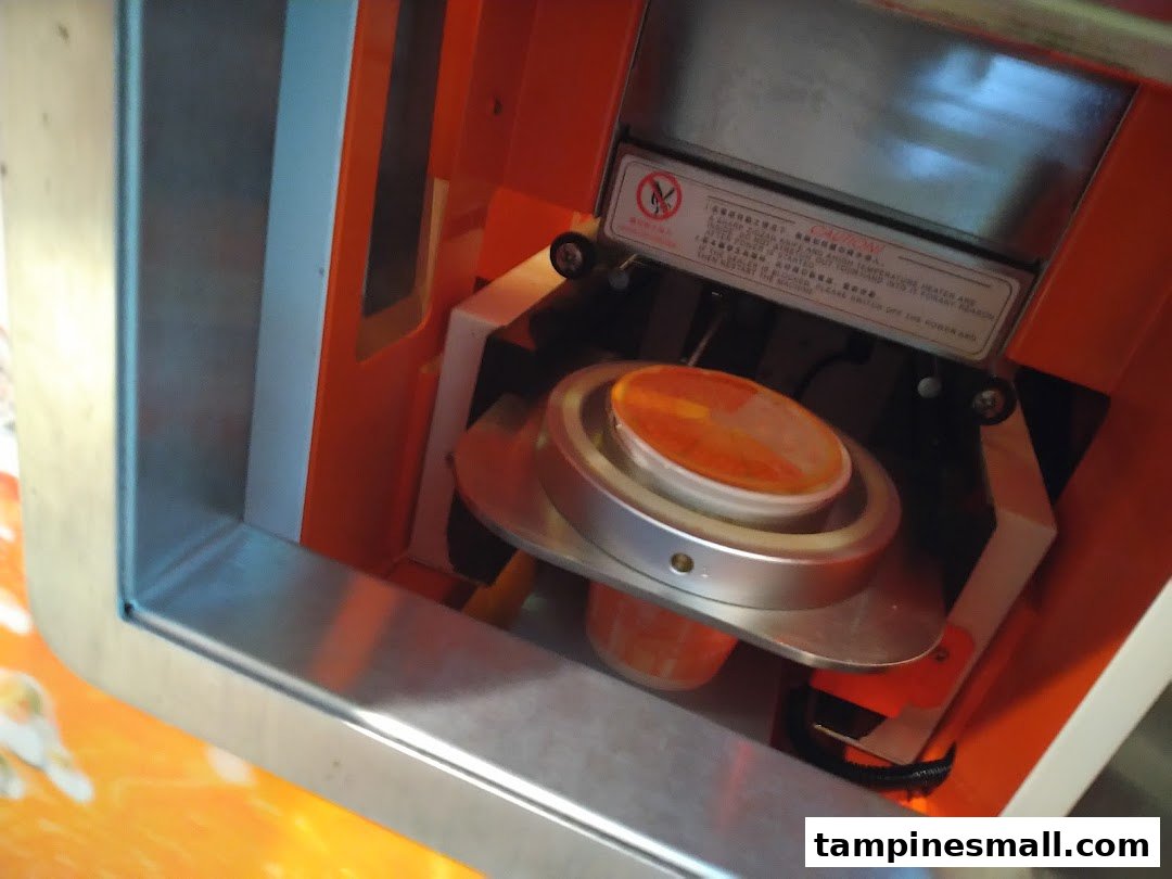 A close-up of a juice cup being sealed by an automated machine at iJooz.