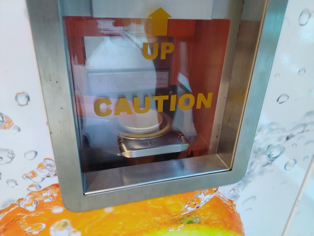 Close-up of an iJooz fresh juice vending machine's dispensing area with 'UP' and 'CAUTION' labels.