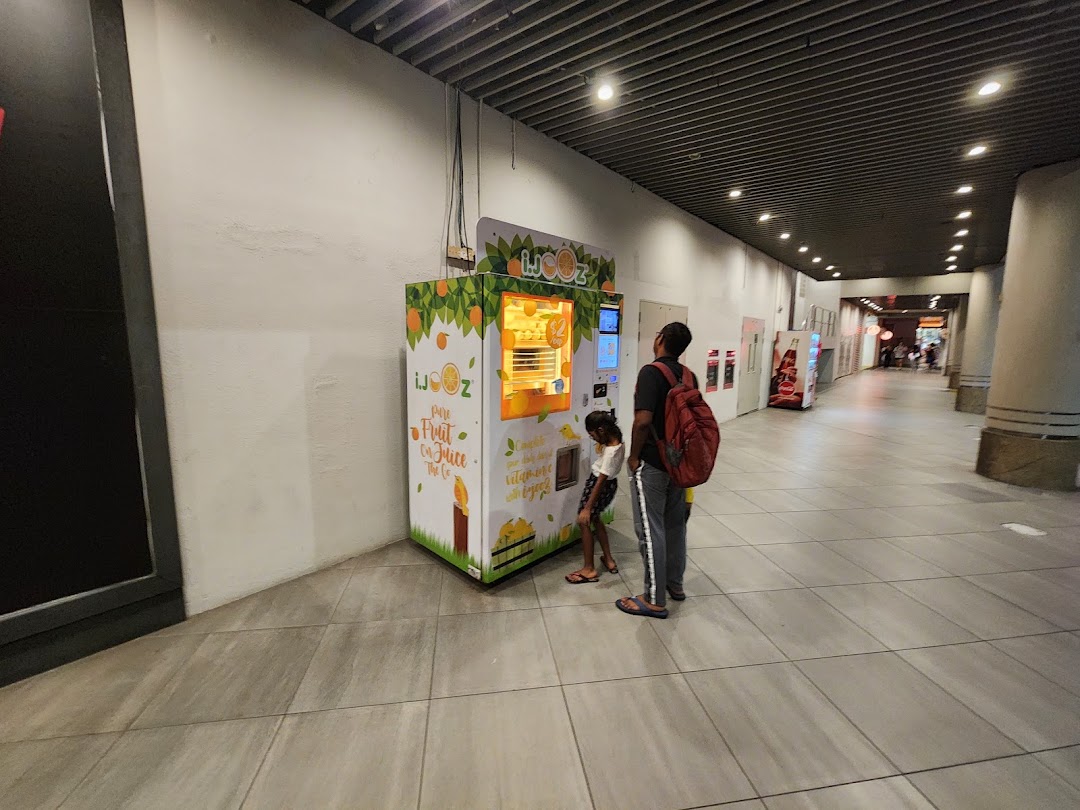 A man and child interact with an iJooz fresh orange juice vending machine in a mall corridor.