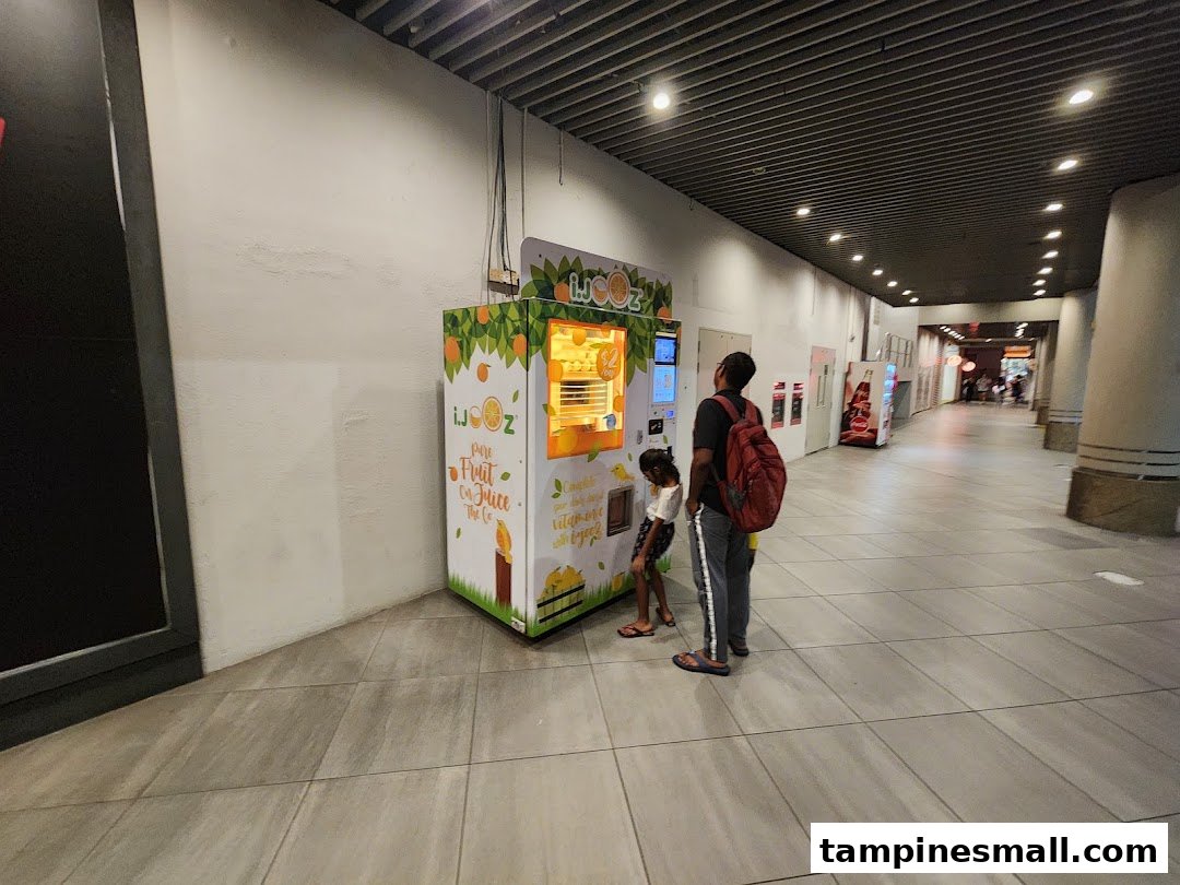 A man and child interact with an iJooz fresh orange juice vending machine in a mall corridor.