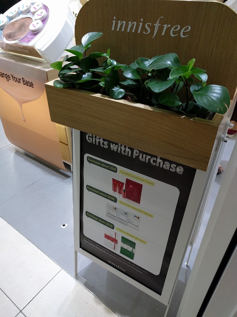 An Innisfree display stand featuring lush green plants and a 'Gifts with Purchase' promotion.