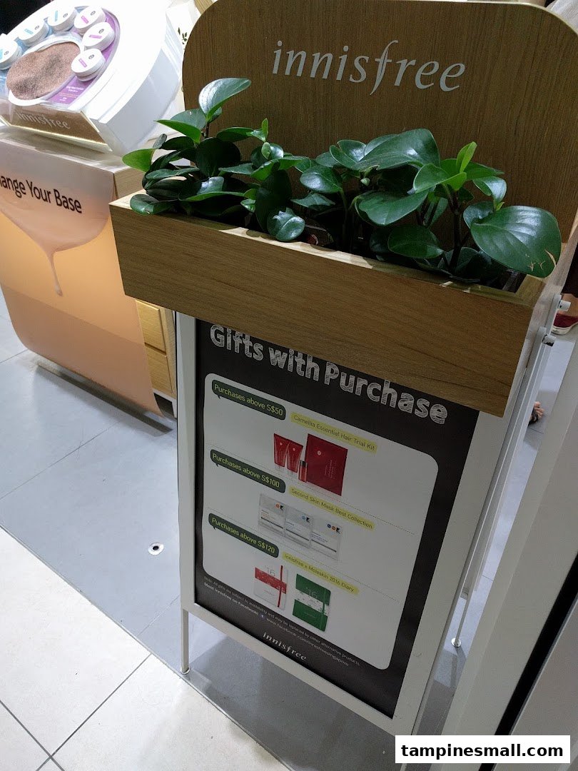 An Innisfree display stand featuring lush green plants and a 'Gifts with Purchase' promotion.