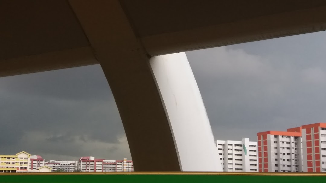 View of distant buildings under a cloudy sky, framed by large architectural structures.