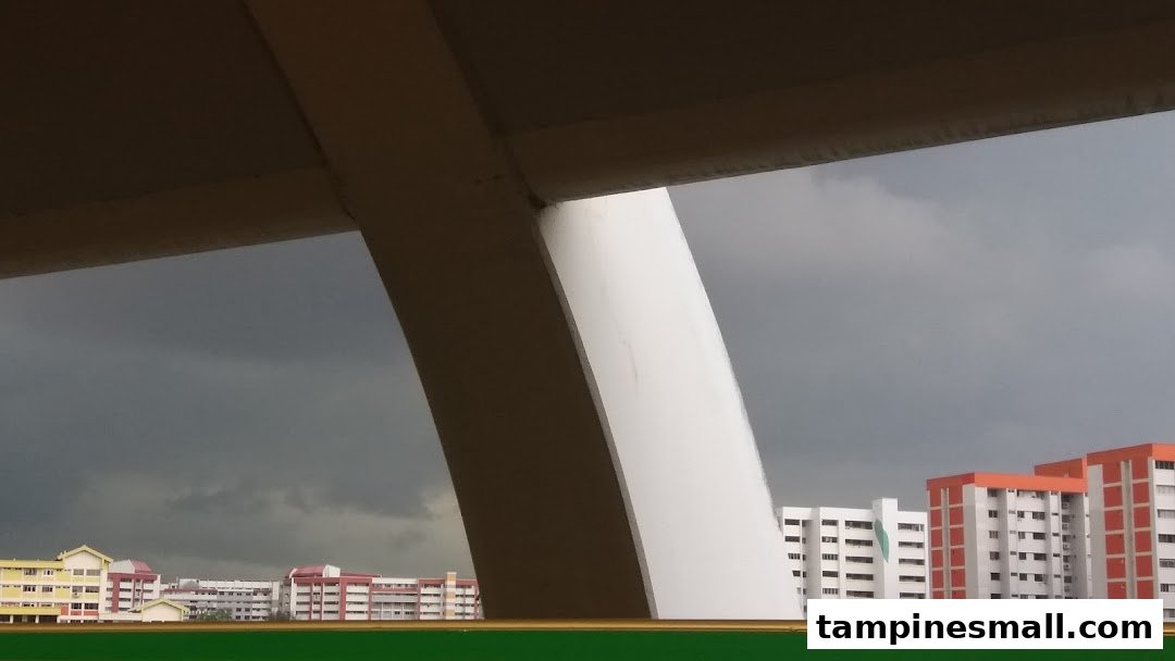 View of distant buildings under a cloudy sky, framed by large architectural structures.