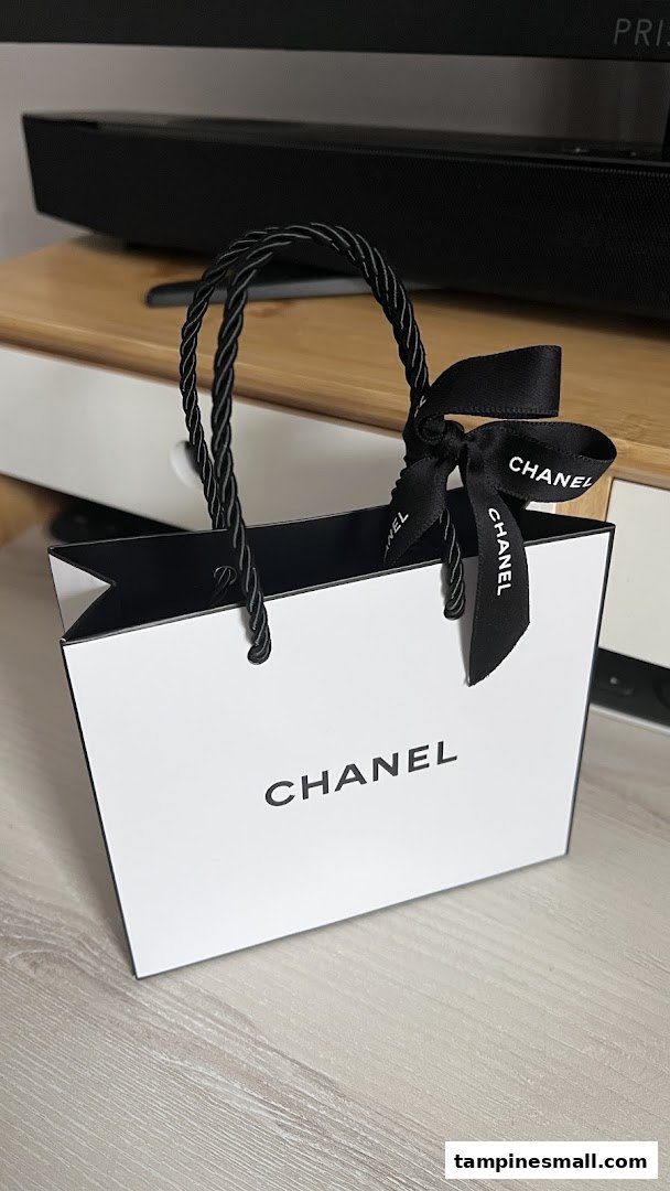 A white Chanel shopping bag with black handles and ribbon, featuring the brand logo.