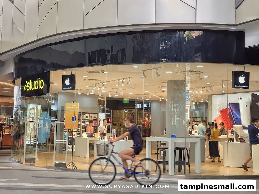 The glass facade of iStudio, an Apple Premium Reseller, with customers inside and a cyclist passing by.