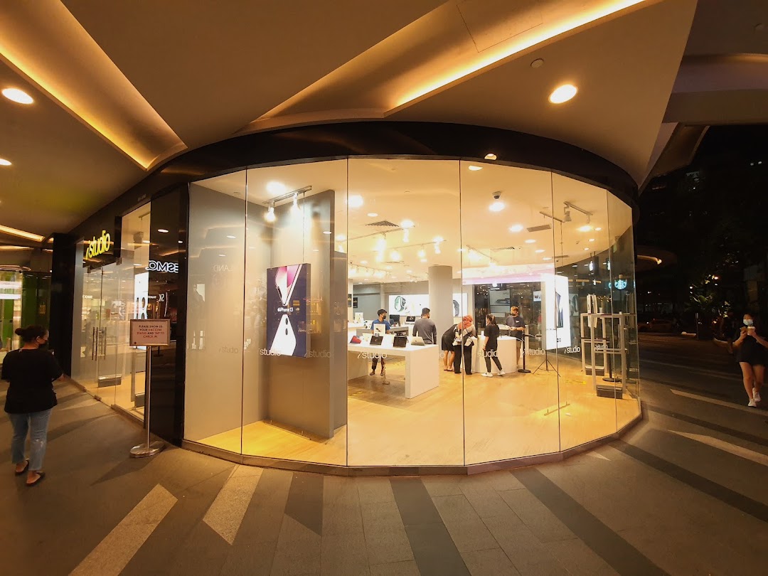 The brightly lit iStudio store with a curved glass facade, showcasing electronics and customers inside.