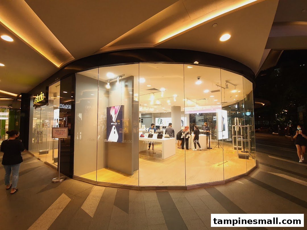 The brightly lit iStudio store with a curved glass facade, showcasing electronics and customers inside.