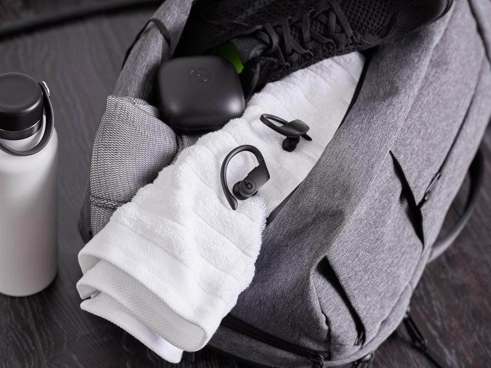 A gym bag packed with Powerbeats Pro earbuds, a water bottle, towel, and athletic shoe.