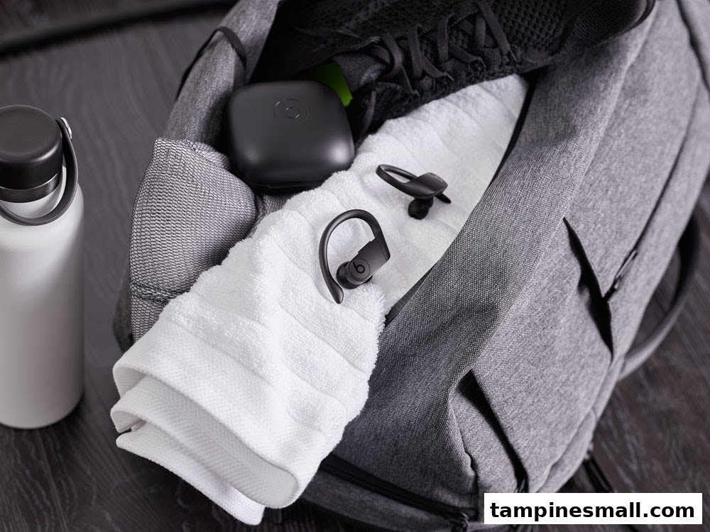 A gym bag packed with Powerbeats Pro earbuds, a water bottle, towel, and athletic shoe.