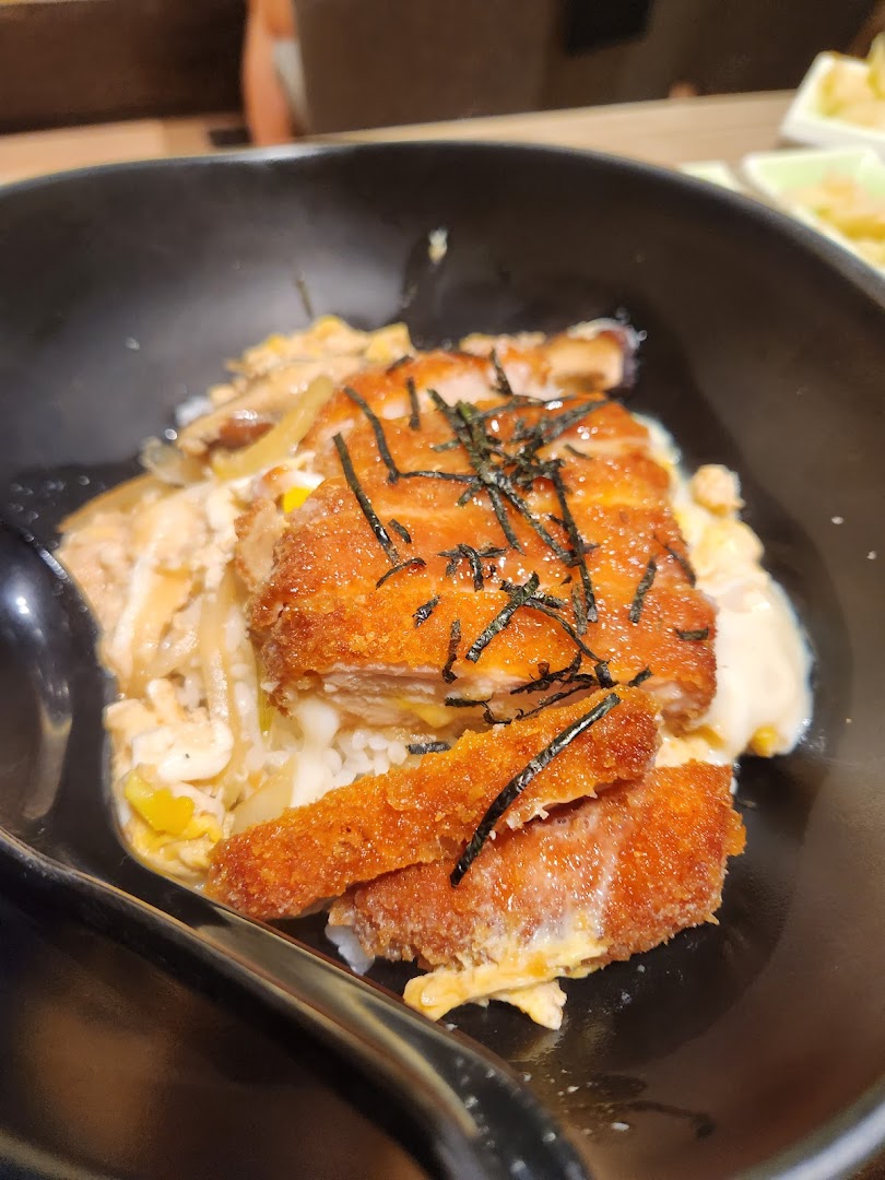 A close-up of a delicious katsu don bowl with crispy fried cutlet, egg, rice, and seaweed.