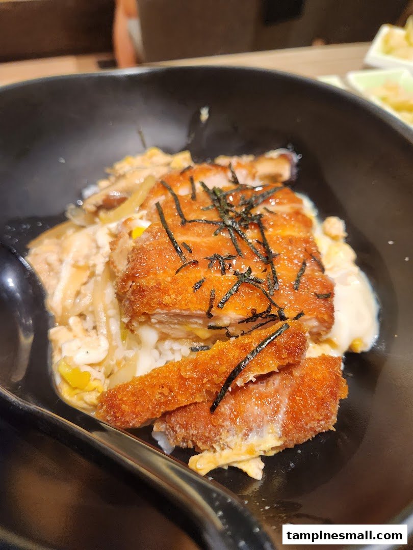 A close-up of a delicious katsu don bowl with crispy fried cutlet, egg, rice, and seaweed.
