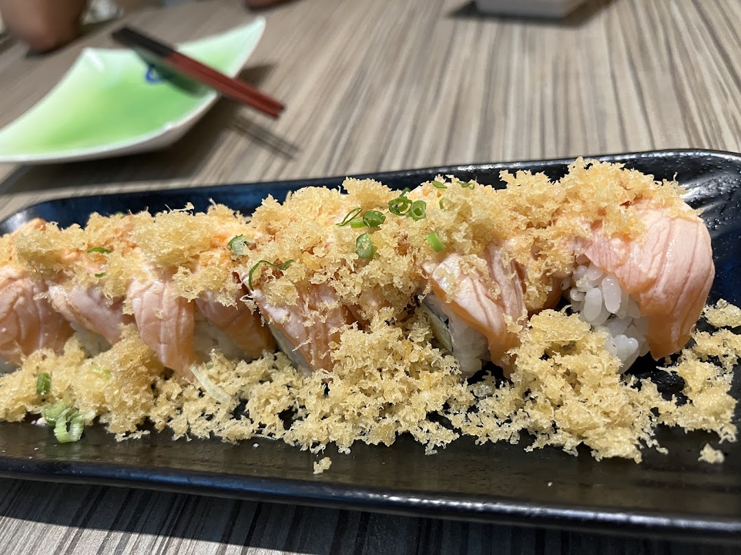 A close-up of delicious salmon sushi rolls topped with crispy tempura flakes and green onions.