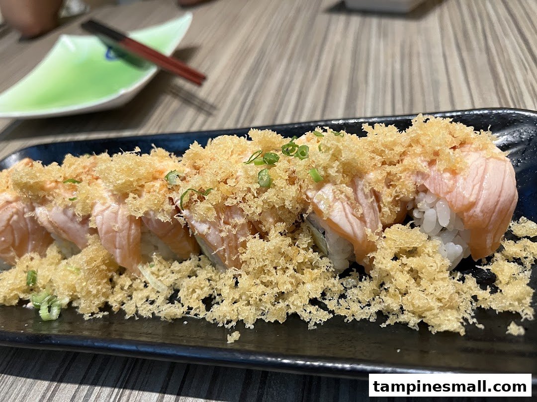 A close-up of delicious salmon sushi rolls topped with crispy tempura flakes and green onions.