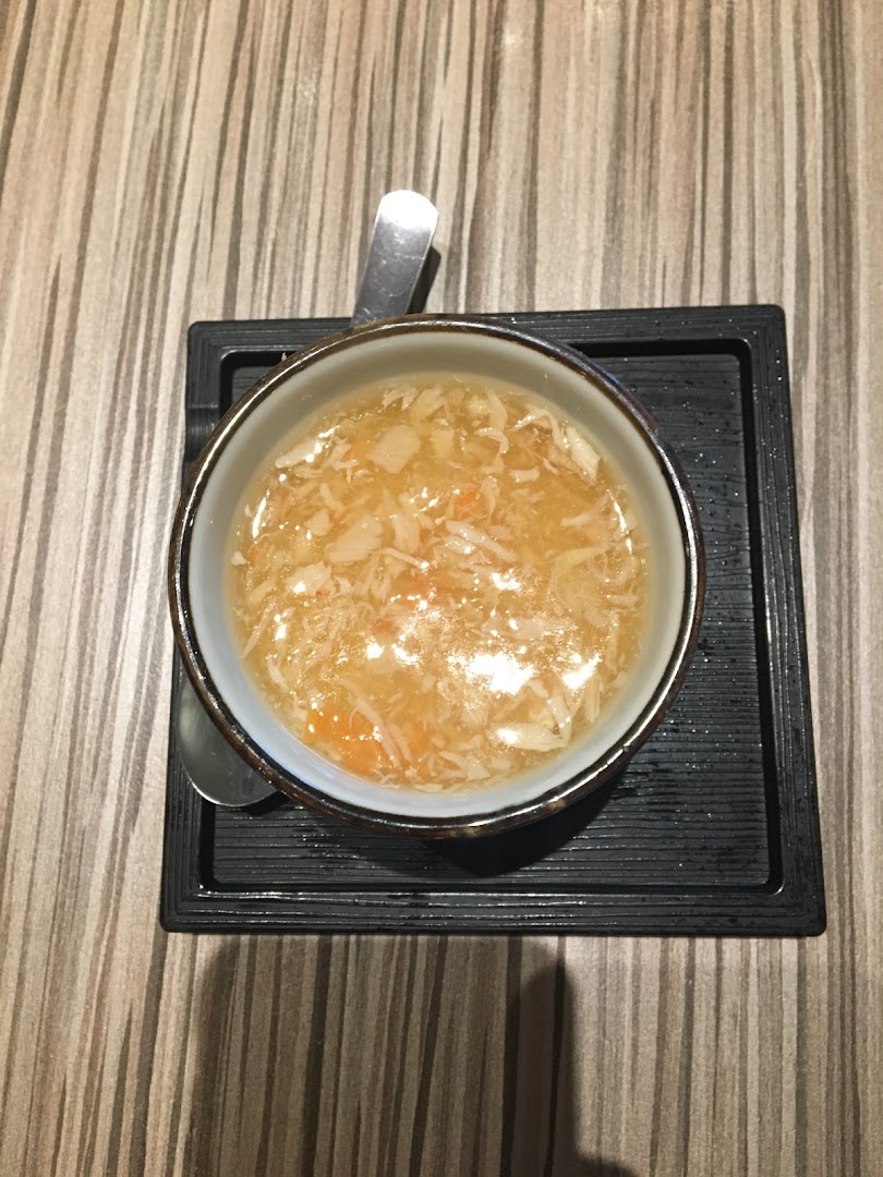 A close-up overhead shot of a bowl of savory soup with shredded ingredients on a wooden table.