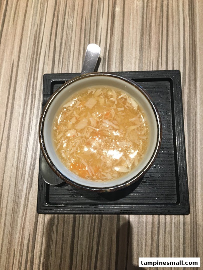 A close-up overhead shot of a bowl of savory soup with shredded ingredients on a wooden table.