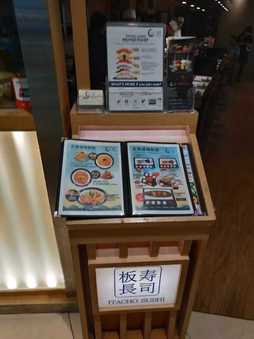 A display stand at Itacho Sushi entrance featuring promotional flyers and the shop's illuminated sign.
