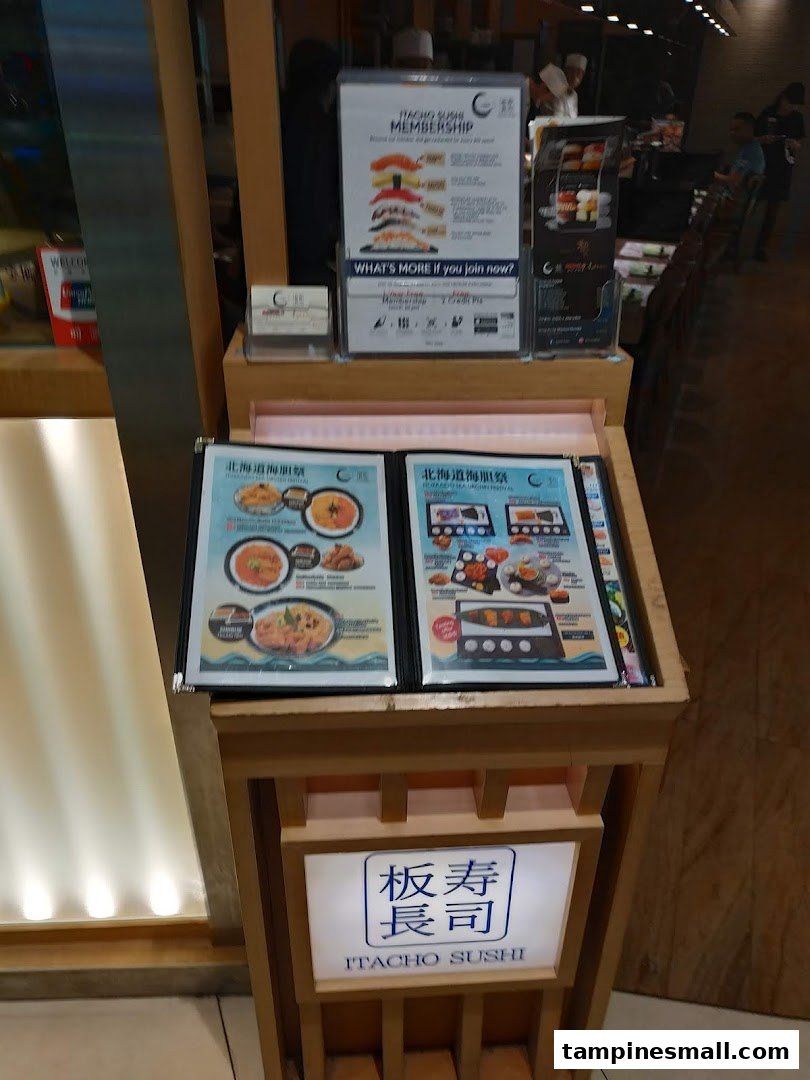 A display stand at Itacho Sushi entrance featuring promotional flyers and the shop's illuminated sign.