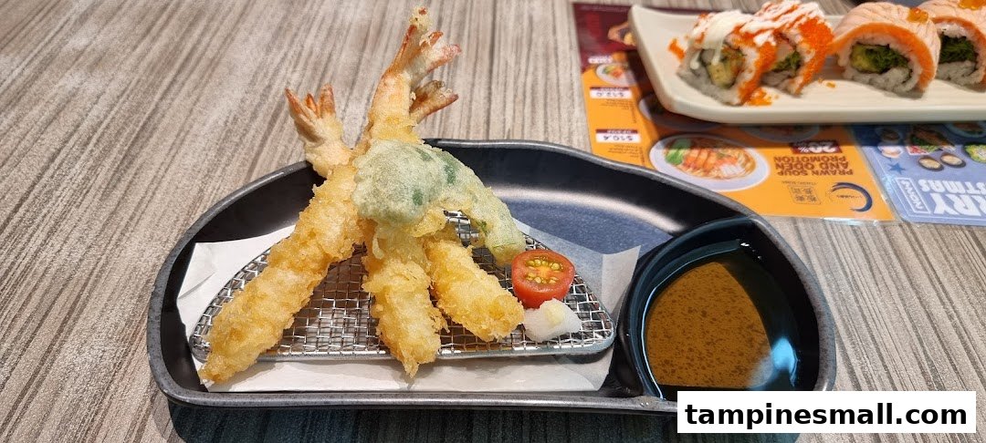 A delicious plate of golden tempura shrimp and vegetable with dipping sauce, alongside sushi rolls.
