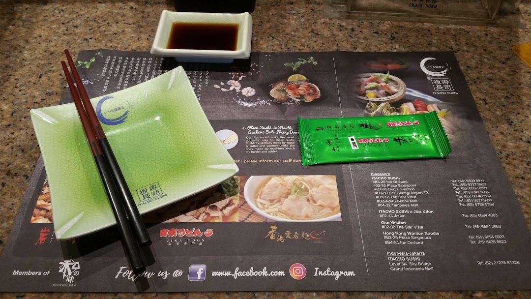 A table setting at Itacho Sushi featuring chopsticks, a plate, soy sauce, and a branded placemat.