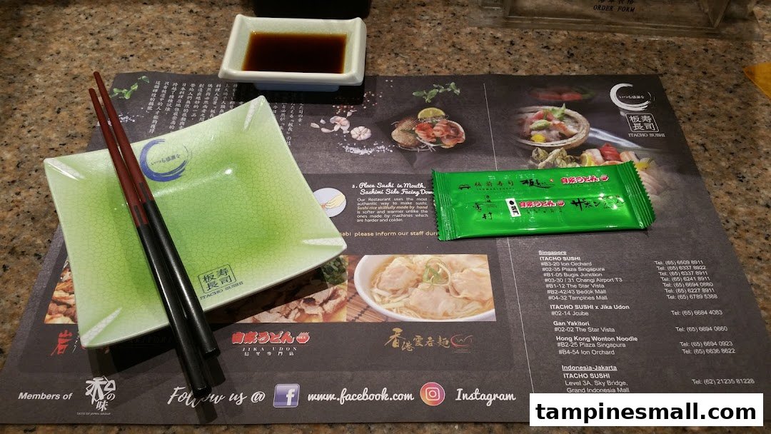 A table setting at Itacho Sushi featuring chopsticks, a plate, soy sauce, and a branded placemat.