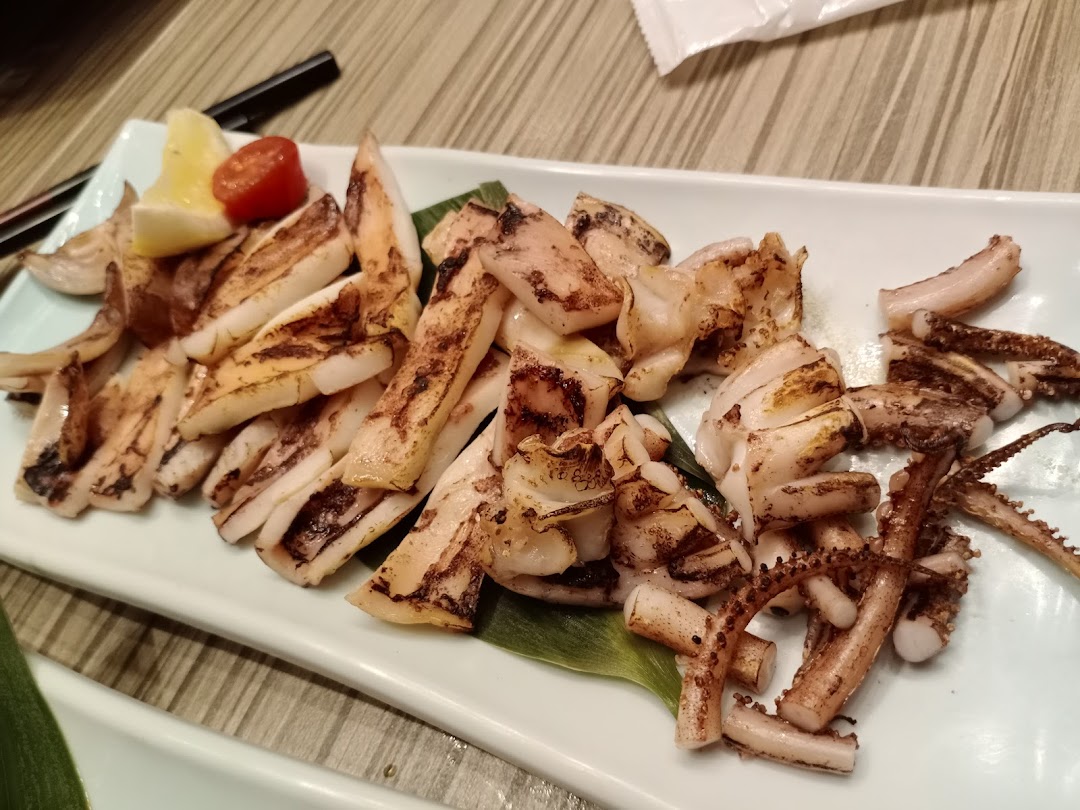 A plate of perfectly grilled squid or calamari, garnished with lemon and a cherry tomato.