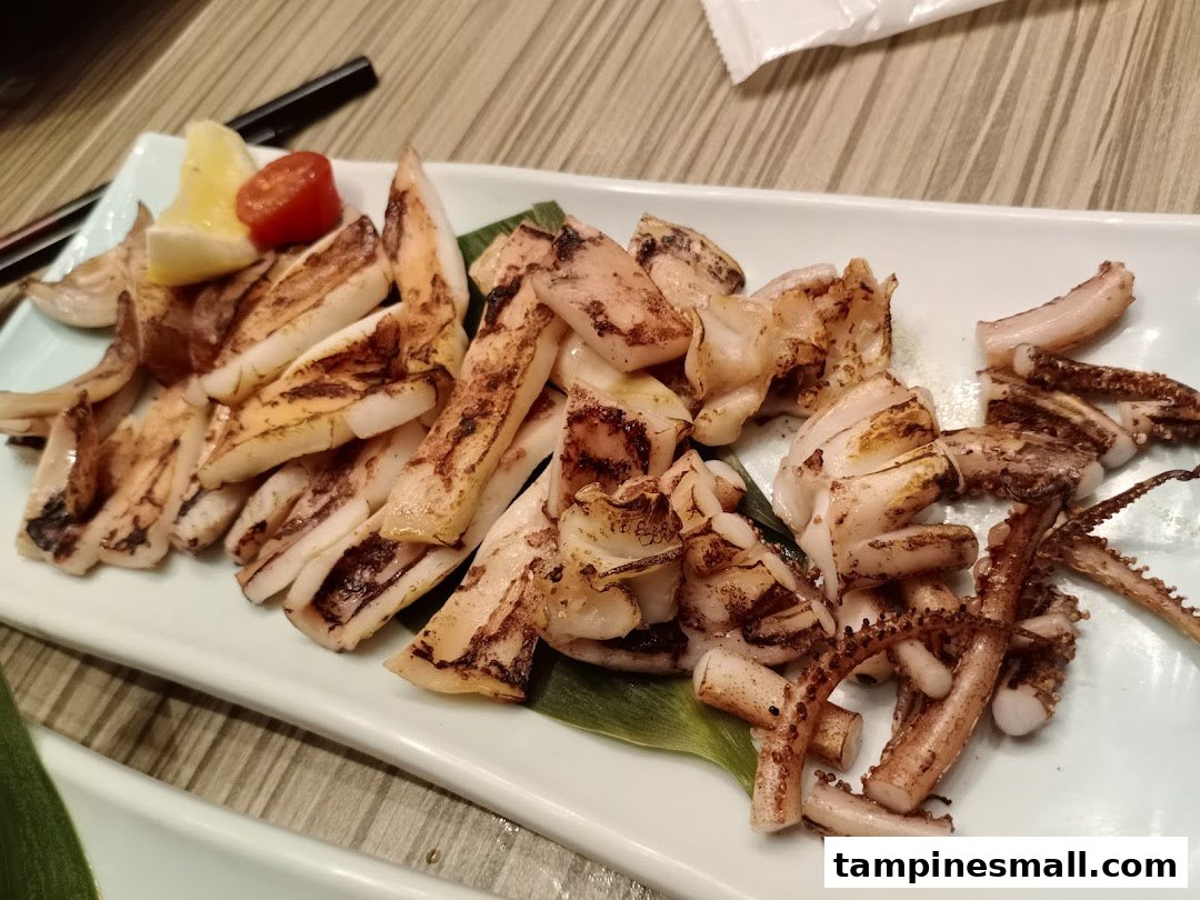 A plate of perfectly grilled squid or calamari, garnished with lemon and a cherry tomato.
