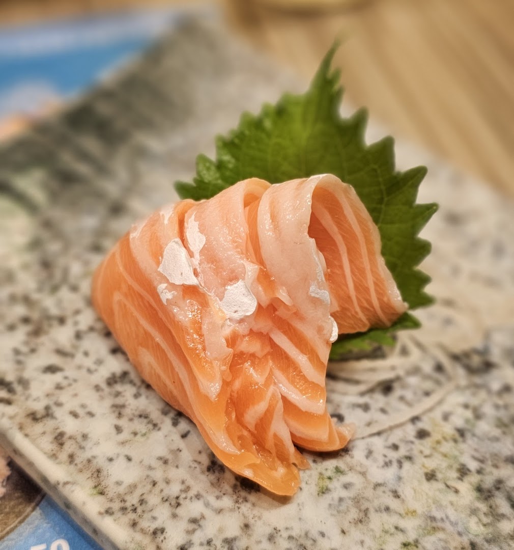 Close-up of fresh salmon sashimi slices served on a speckled plate with a green shiso leaf.