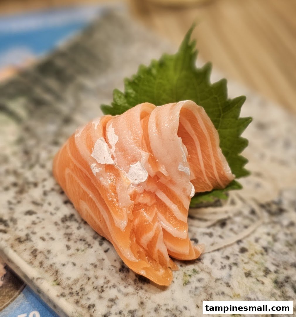 Close-up of fresh salmon sashimi slices served on a speckled plate with a green shiso leaf.