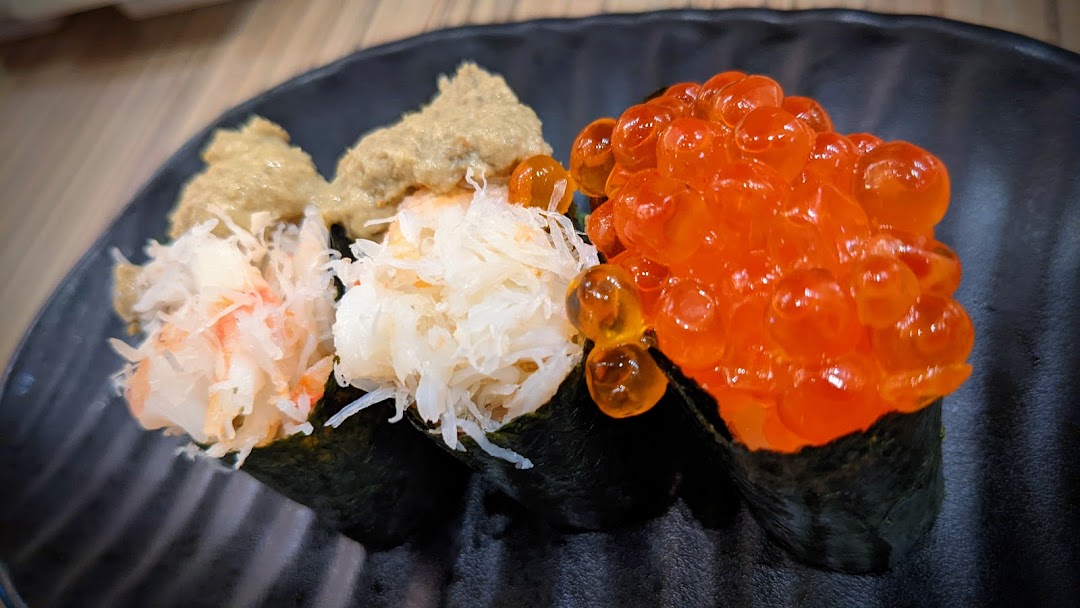 A close-up of three gourmet sushi pieces, including crab meat and salmon roe, on a black plate.