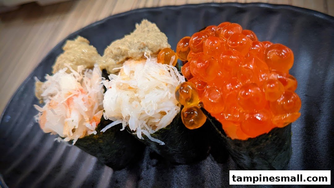 A close-up of three gourmet sushi pieces, including crab meat and salmon roe, on a black plate.