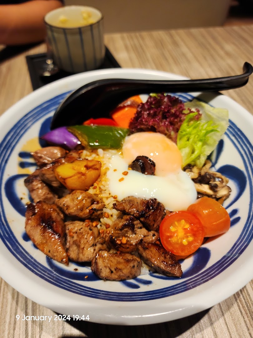 A close-up of a delicious beef donburi bowl with a poached egg, vegetables, and rice.