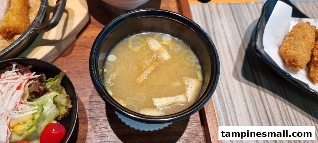 A close-up of a Japanese meal featuring miso soup, a fresh salad, and crispy fried items.