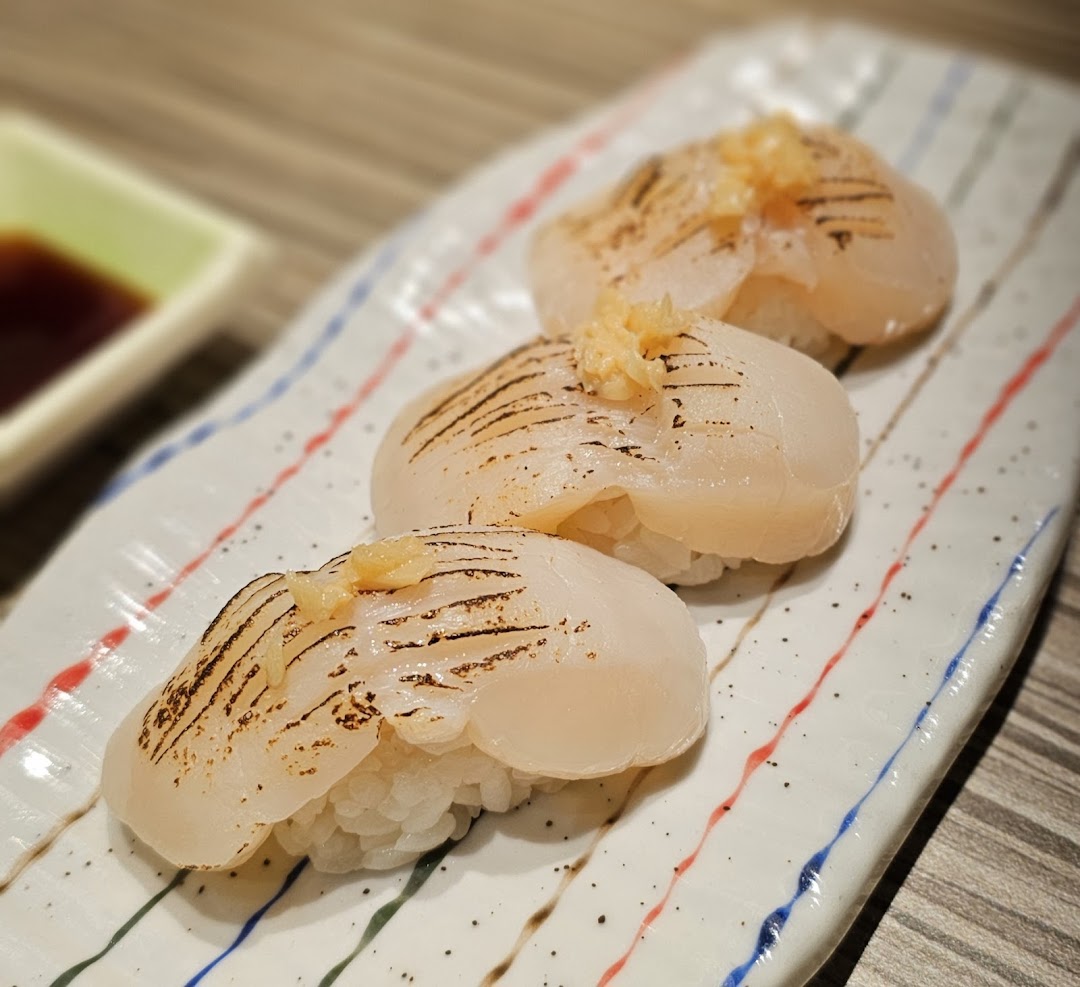 Three pieces of perfectly seared scallop sushi with a hint of garnish on a decorative plate.