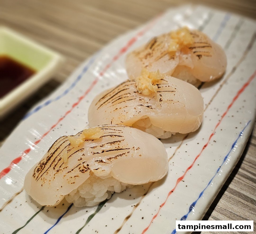 Three pieces of perfectly seared scallop sushi with a hint of garnish on a decorative plate.
