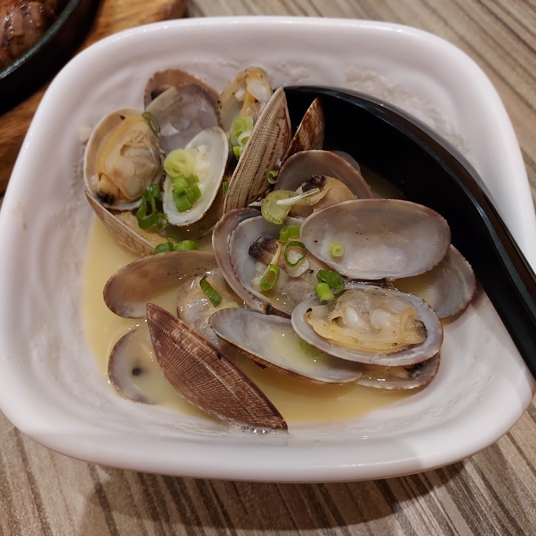 A white bowl filled with steamed clams in a light broth, garnished with chopped green onions.