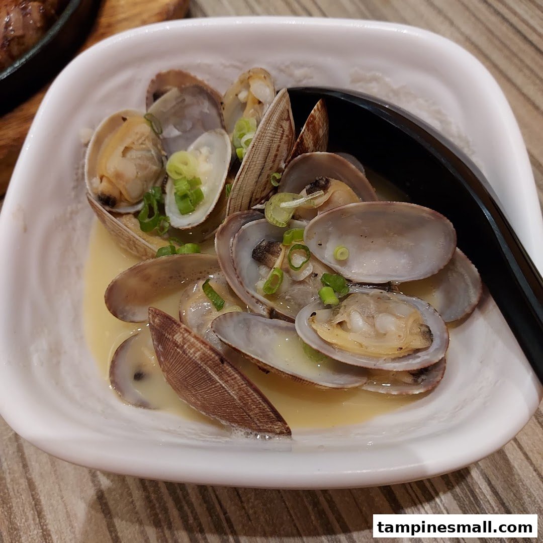 A white bowl filled with steamed clams in a light broth, garnished with chopped green onions.