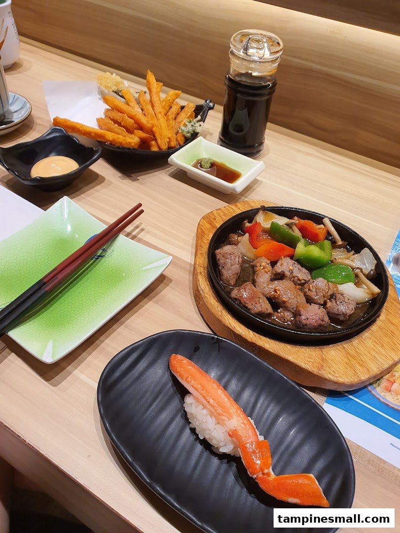 A table laden with various Japanese dishes including sushi, sweet potato fries, and sizzling beef.