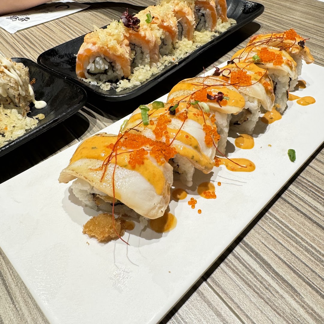 Close-up of two plates of gourmet sushi rolls, featuring various toppings and sauces.