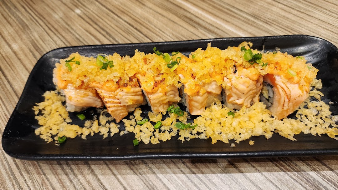 A close-up of a delicious salmon sushi roll topped with crispy tempura flakes and green onions.