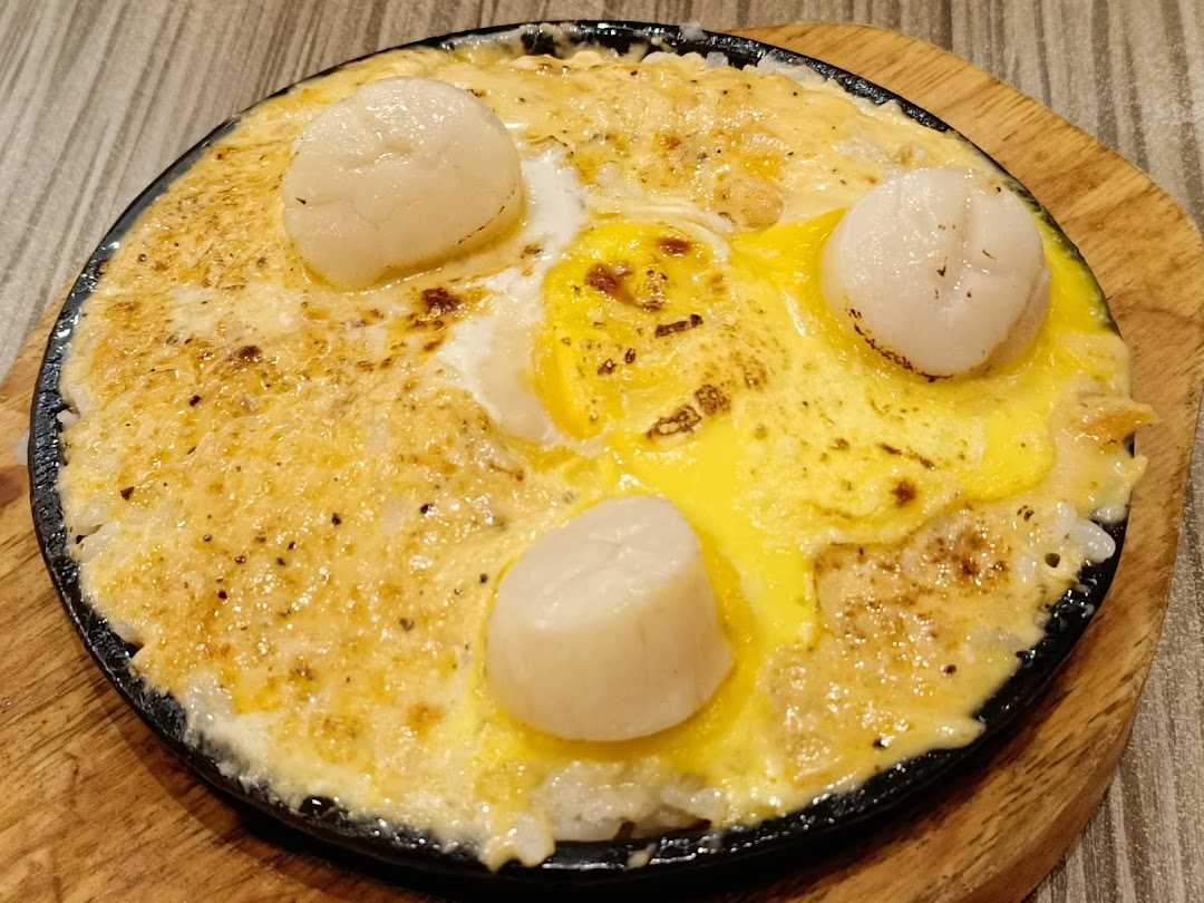 A sizzling hot plate dish featuring scallops, melted cheese, and a sunny-side-up egg.