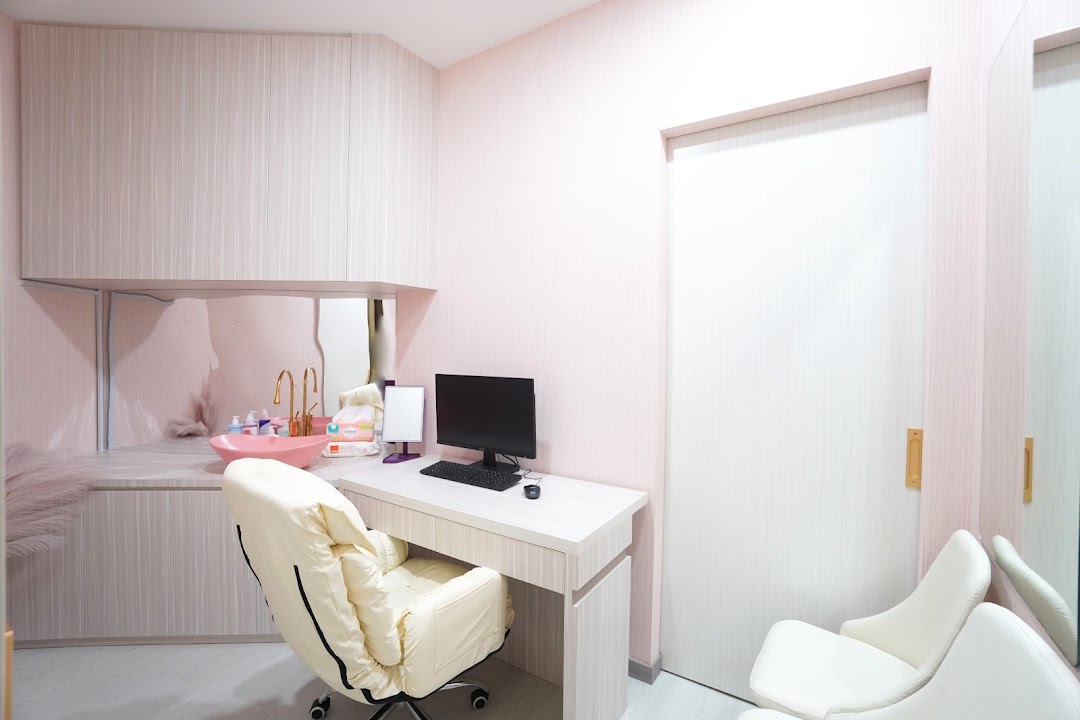 A modern, pink-themed medical clinic room with a desk, computer, sink, and comfortable chairs.