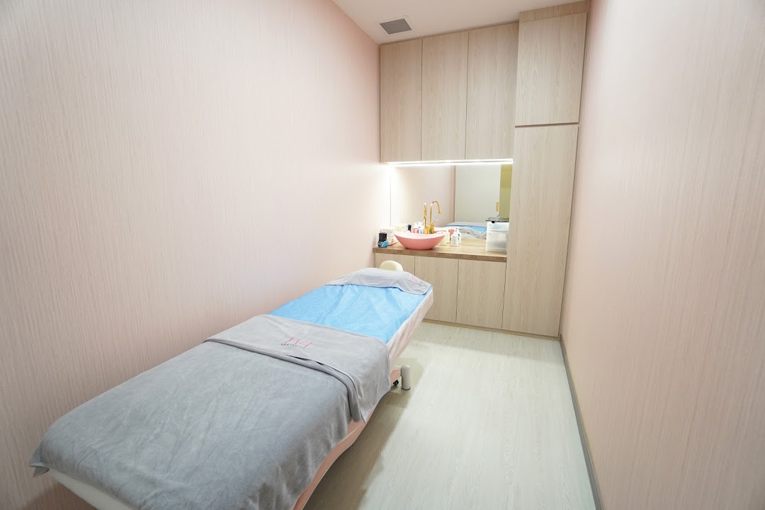 A clean, modern treatment room with a bed and sink, featuring light pink walls and wooden cabinetry.