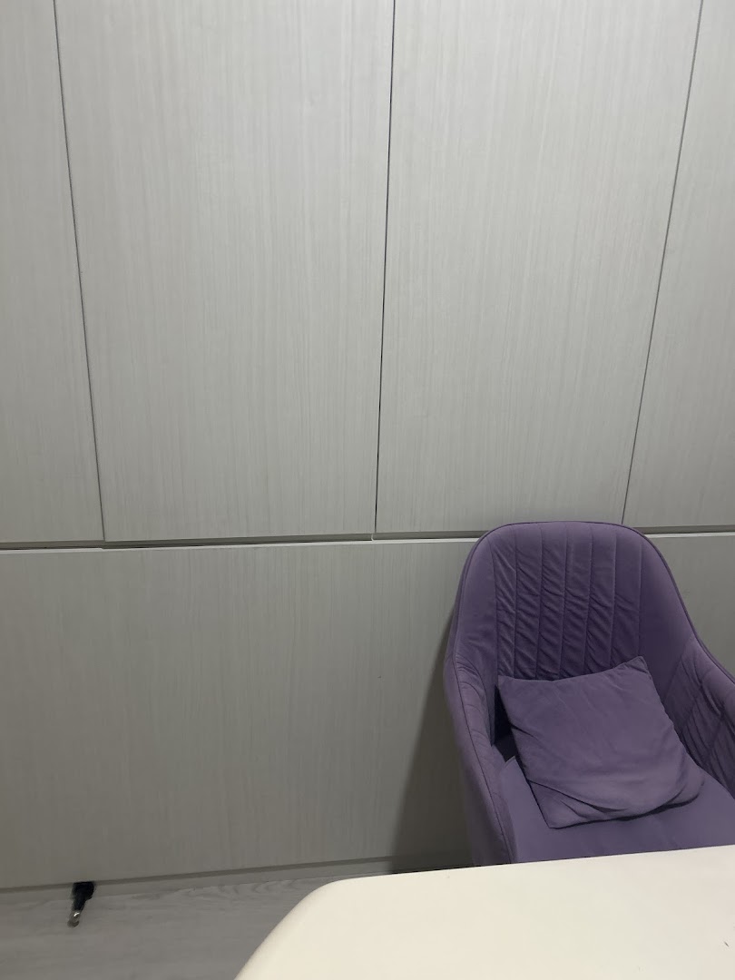 A comfortable purple armchair with a cushion next to light wood paneling and a white table.