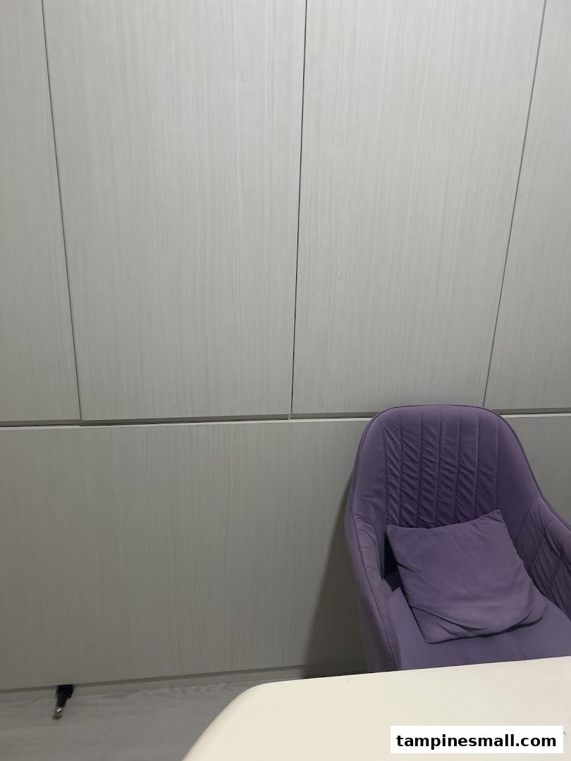 A comfortable purple armchair with a cushion next to light wood paneling and a white table.