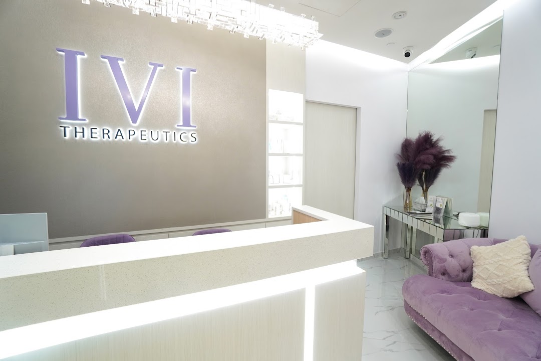 A bright, modern reception area with the 'IVI Therapeutics' logo, a white counter, and a purple velvet sofa.