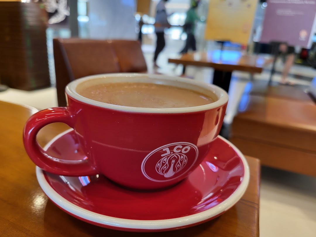 A red J.Co branded coffee cup filled with a beverage on a wooden table.