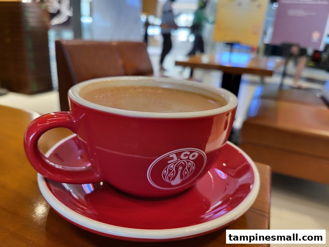 A red J.Co branded coffee cup filled with a beverage on a wooden table.