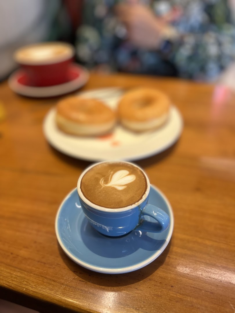 A latte with heart-shaped latte art and two donuts on a wooden table.